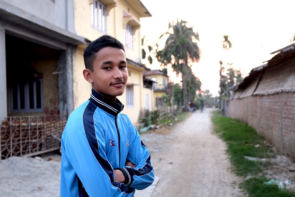 Nepalilainen poika seisoo ulkona ja katsoo kameraan.