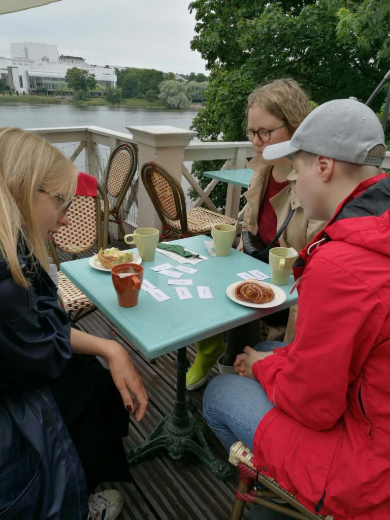 Kolme henkilöä istuu kahvilapöydän ääressä ulkoterassilla.