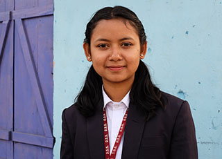 A girl in a black and white school uniform in front of a light blue wall.
