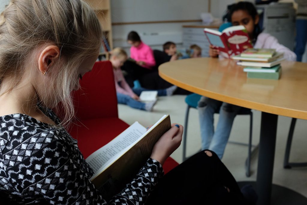 Lapsia koulun tiloissa lukemassa kirjoja.