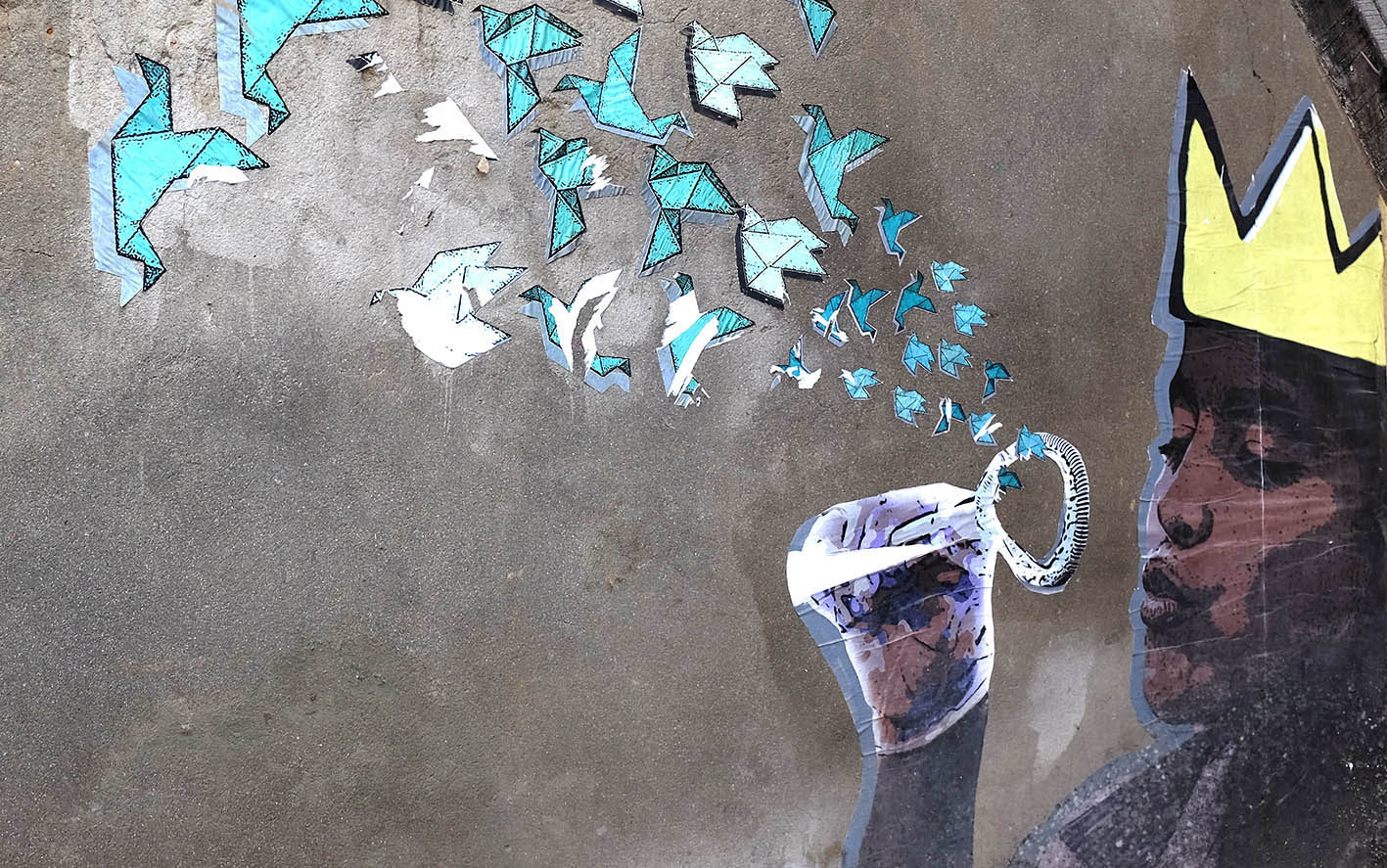 Seinämaalauksessa kruunupäinen lapsi puhaltaa origamilintujen muotoisia saippuakuplia.