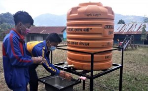 2 poikaa pesee käsiä ulkona ison vesitankin edessä.