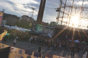 Kuva festivaalialueesta, jossa satoja ihmisiä aukealla auringon laskiessa taustalla.