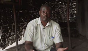 Mies lyhythihaisessa vaaleassa kauluspaidassa puhuu ja katsoo kohti.