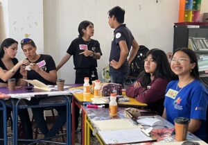 Kuusi nuorta istuu ja seisoo pöytäryhmän ympärillä.