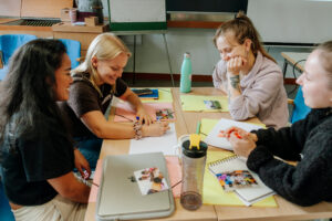 Neljä nuorta aikuista tekee hymyillen ryhmätyötä pöydän ääressä.