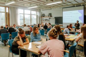 Kuva luokkahuoneesta, jossa 24 nuorta aikuista tekee ryhmätöitä pöytäryhmissä.