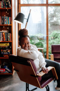 Aggie istuu tuolilla ja katsoo hymyillen kameraan.