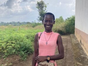 Nuori hymyilevä nainen vaaleanpunaisessa mekossa. Taustalla peltoa.