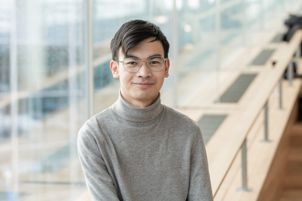 Nuori henkilö hymyilee lähikuvassa, hänellä on harmaa poolopaita ja tummat lyhyet hiukset.