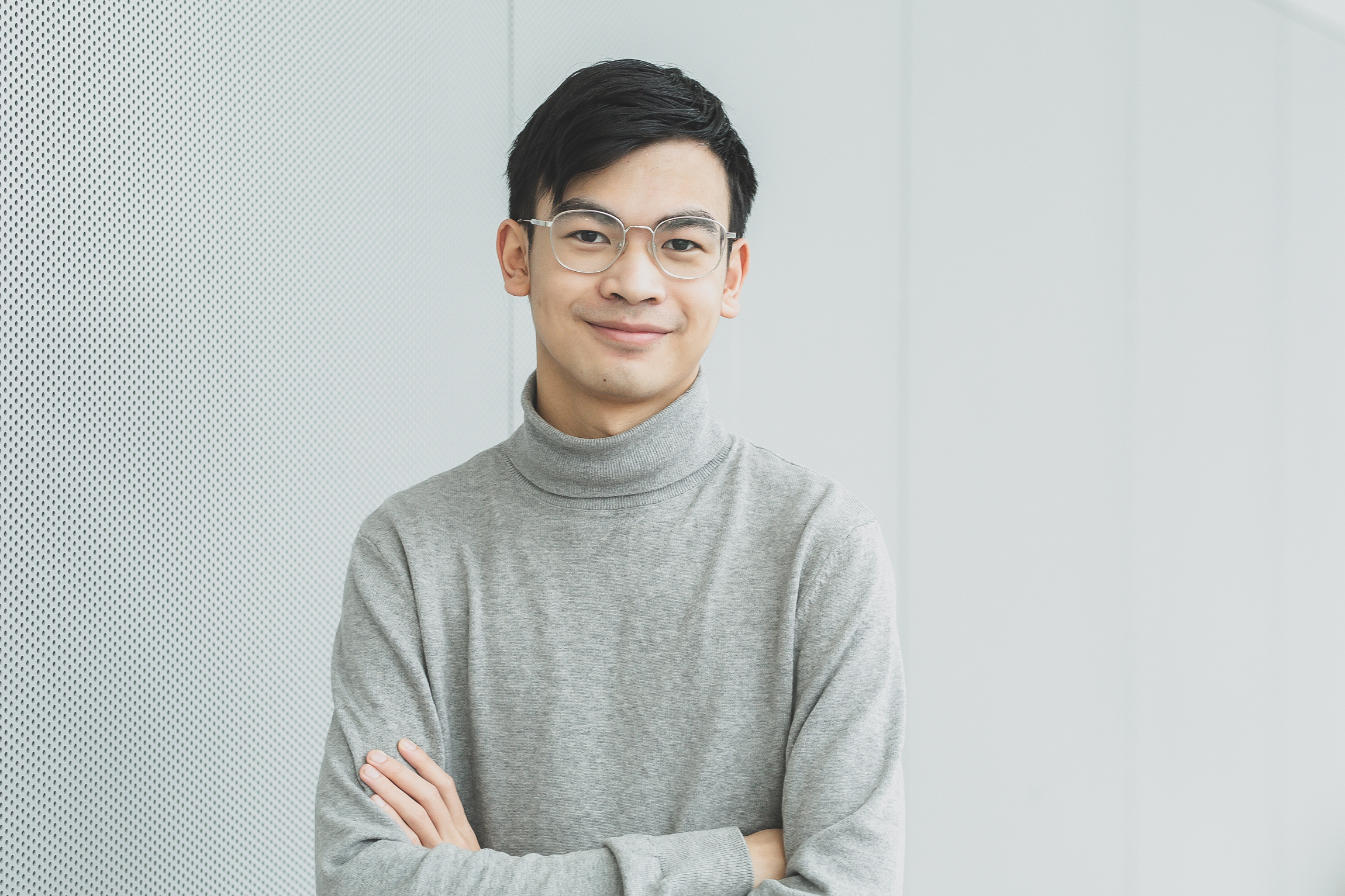 Nuori henkilö hymyilee lähikuvassa, hänellä on harmaa poolopaita ja tummat lyhyet hiukset.