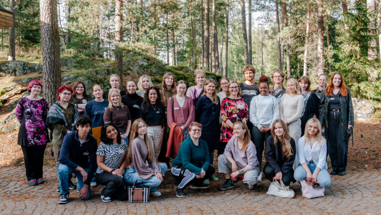 Noin 25 henkilön ryhmä poseeraa kameralle metsän edessä.