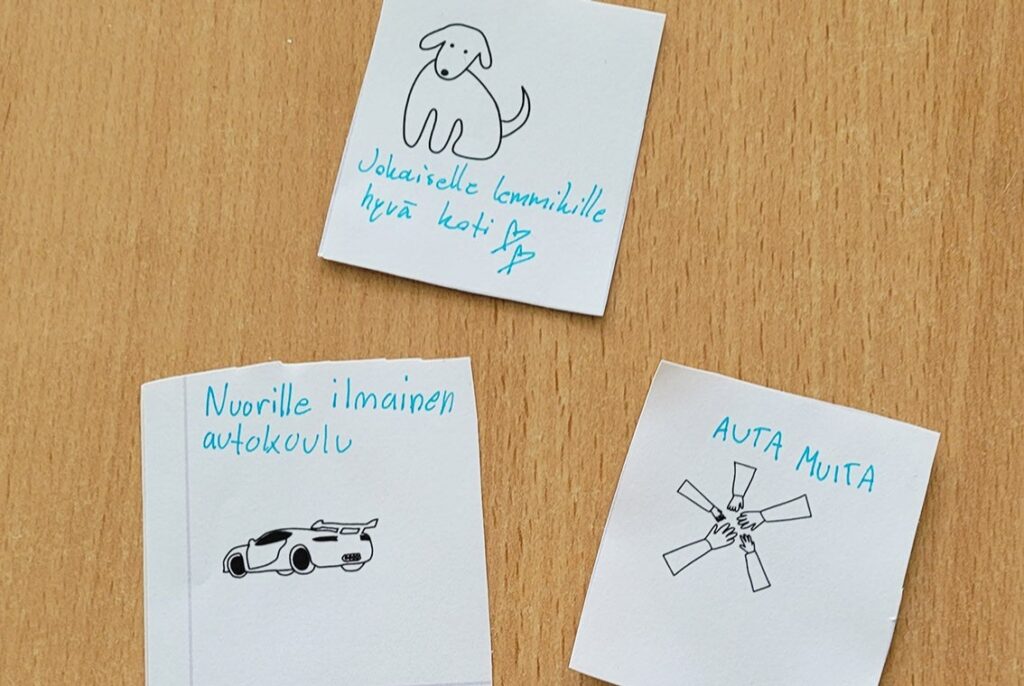 Valkoisilla paperitarroilla on mustia viivapiirroksia ja käsin kirjoitettuja sanoja: Jokaiselle lemmikille hyvä koti. Auta muita. Nuorille ilmainen autokoulu.